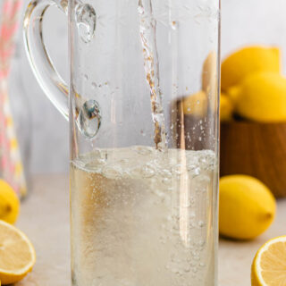 Pouring finished syrup into tall pitcher, lemons in background.
