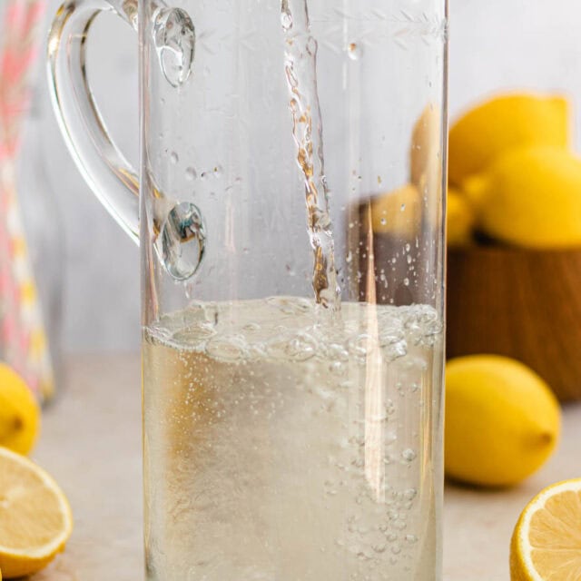 Pouring finished syrup into tall pitcher, lemons in background.
