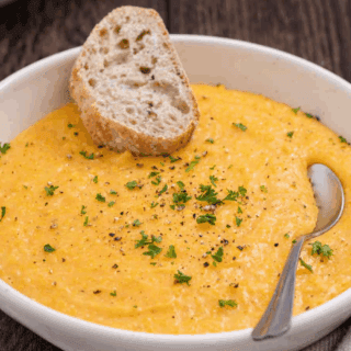 Garnished cooked grits in bowl with spoon and bread piece