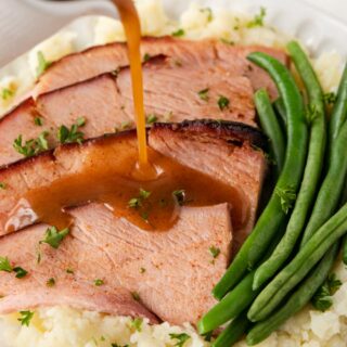 Ham on dinner plate with mashed potatoes and green beans.
