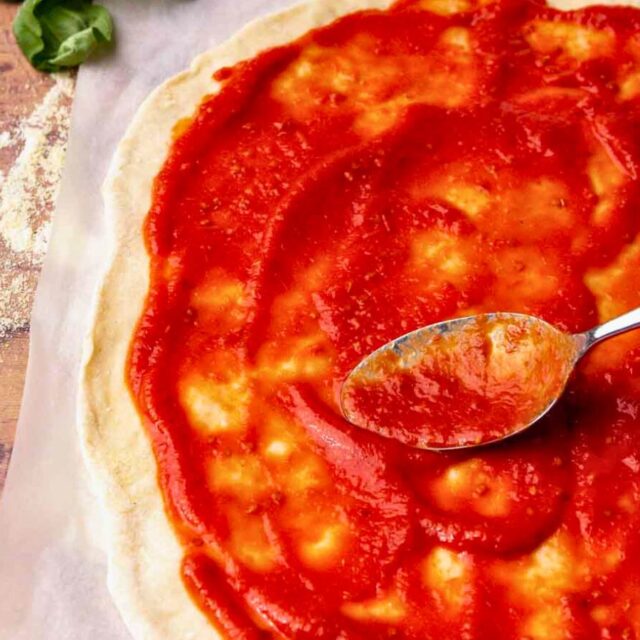 Thin pizza dough with red sauce being spread