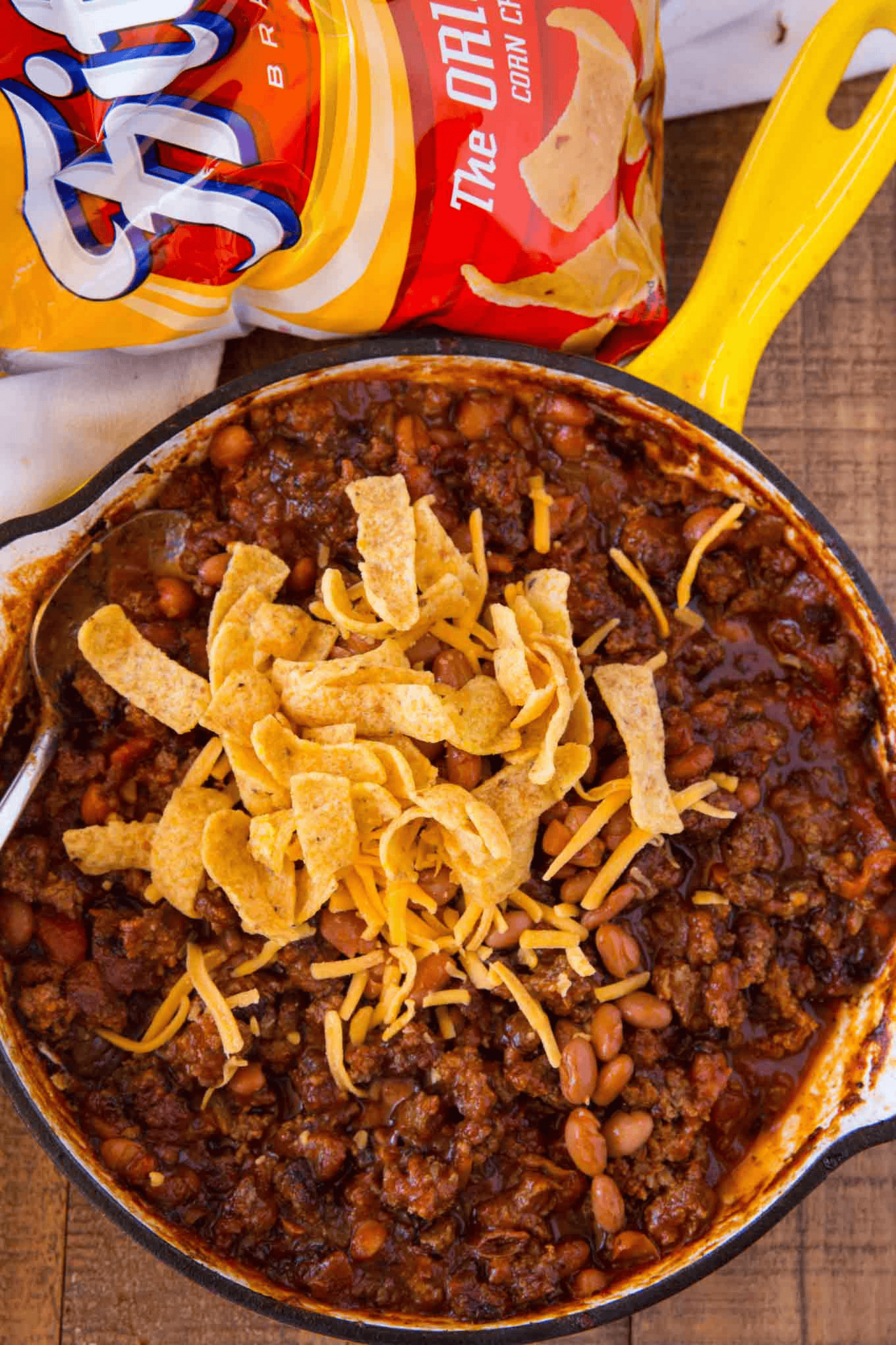 Pan of beans and meat sauce topped with chips and cheese with a bag of chips on the side