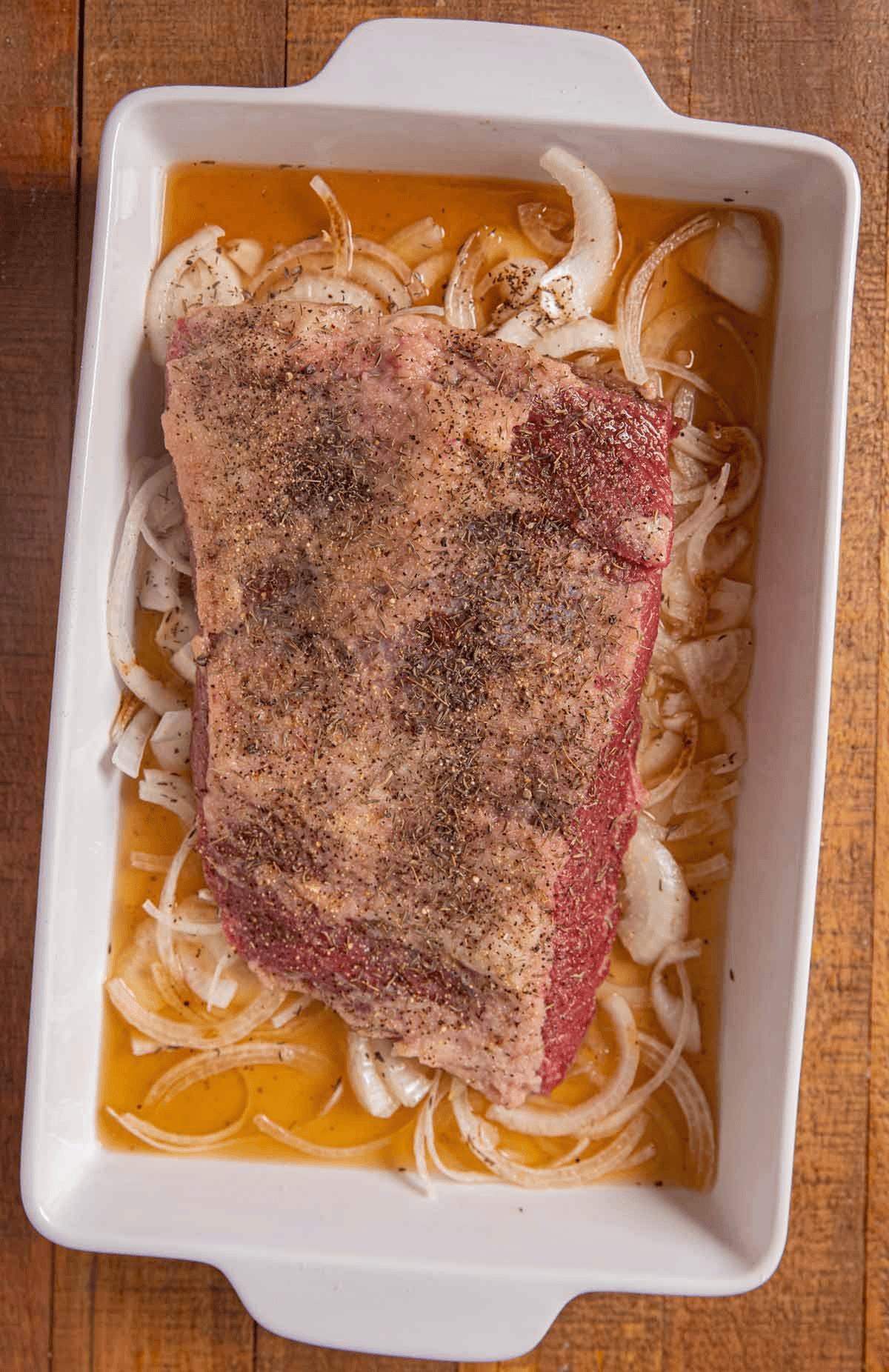 Seasoned brisket in a pan with beer and onion