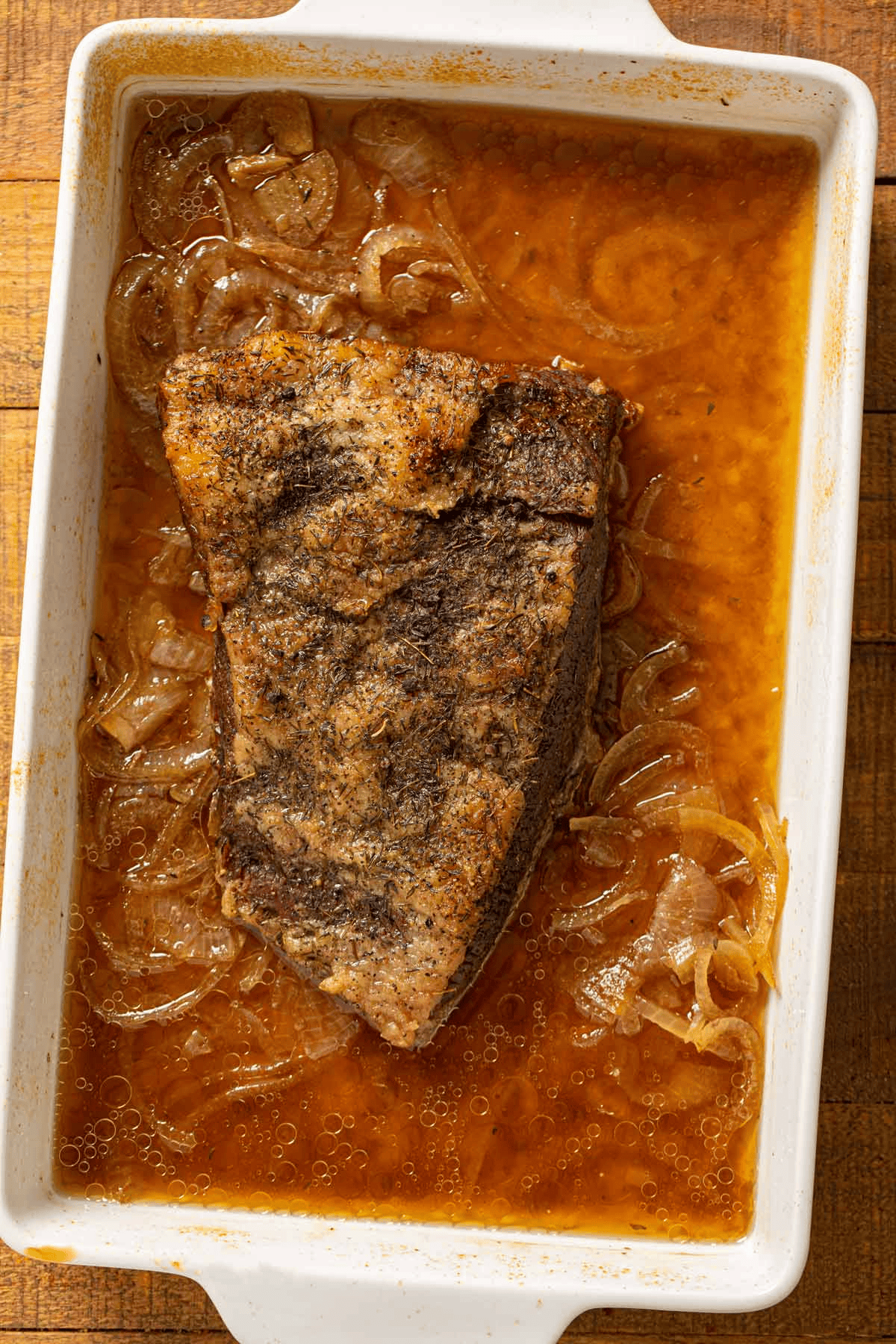 Roasted brisket in a pan with beer and onion at the bottom