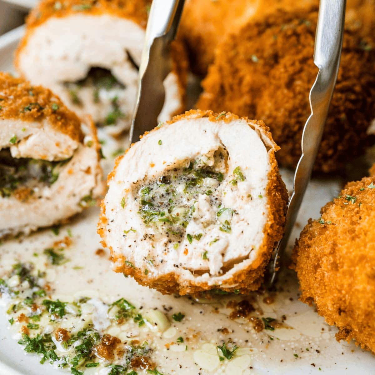 Tongs picking up stuffed piece of chicken, sliced so filling shows