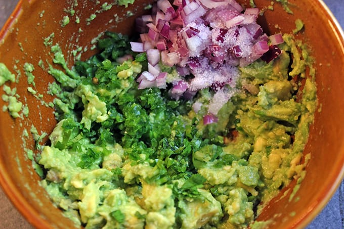 Mashed avocado, red onion, and seasoning ingredients unmixed in a bowl
