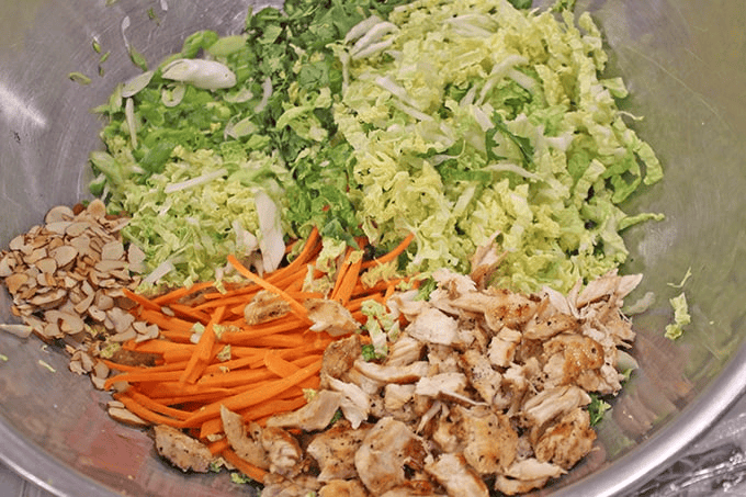 carrots, almonds, cabbage, and chicken pieces in a metal bowl