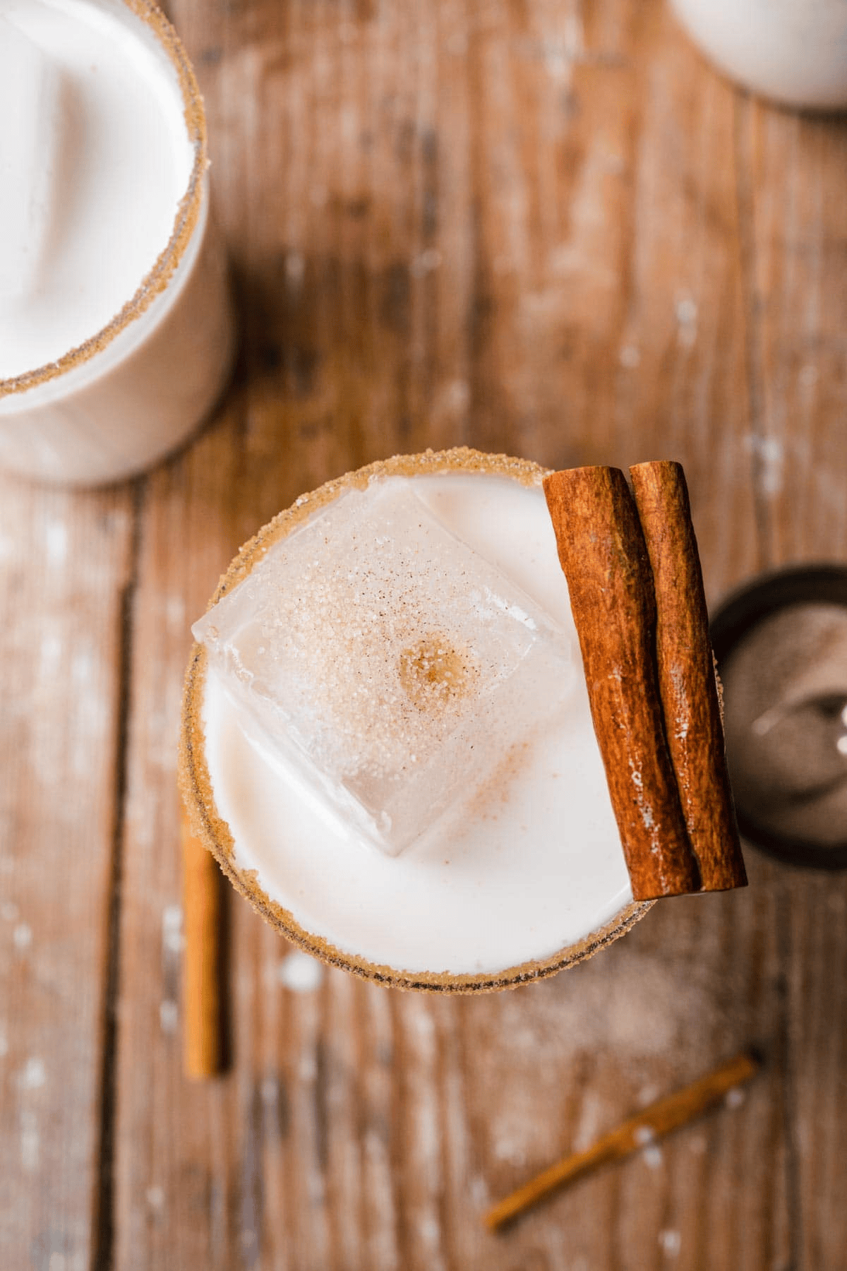 Creamy drink shown from above with ice cube and cinnamon stick on top