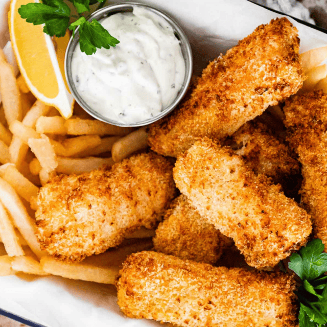 cooked breaded fish on a plate with a white sauce, french fries and lemon slice