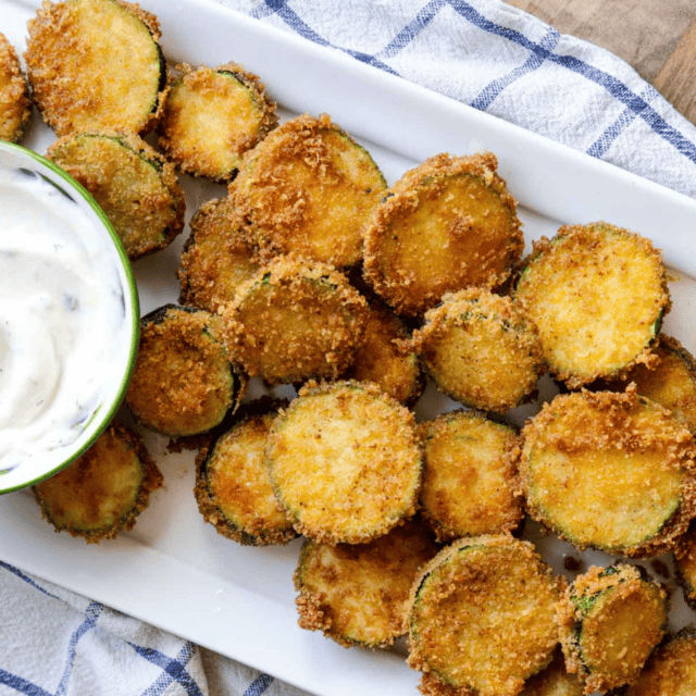 Fried round vegetable on a white platter with a bowl of white dipping sauce