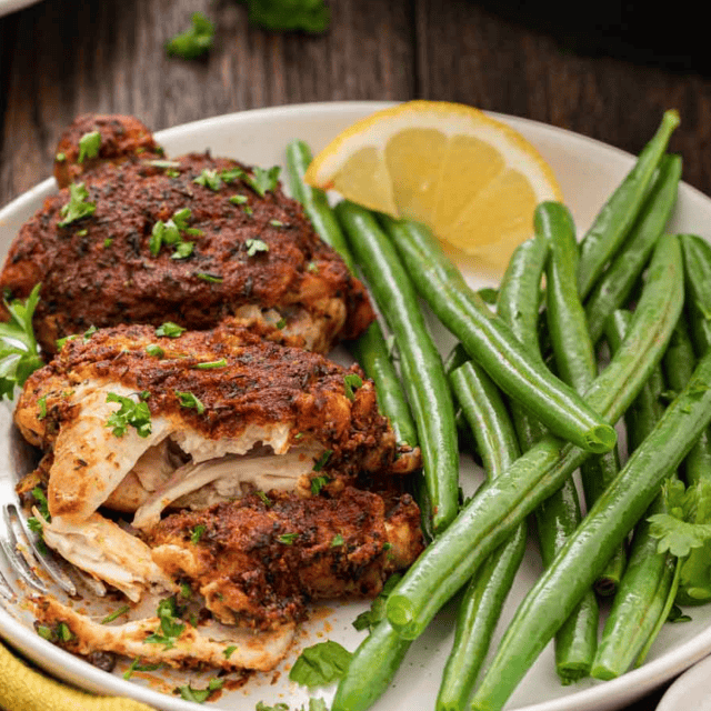 Season poultry on a plate with green beans and a wedge of lemon on a white plate.