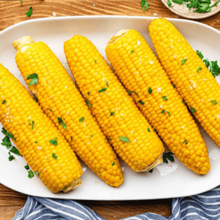 Cooked and garnished whole corn cobs on serving plate