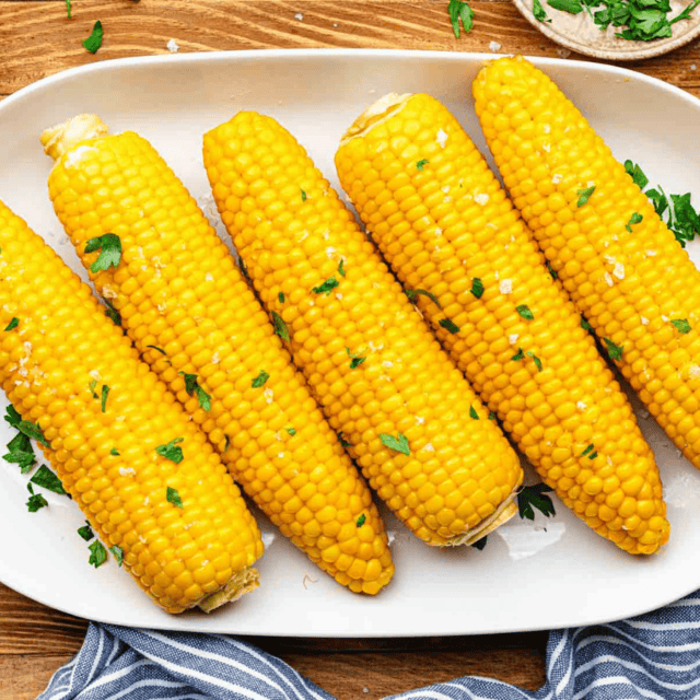 Cooked and garnished whole corn cobs on serving plate