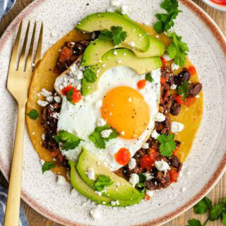 Sunny side egg, tomatoes and beans on tostada with avocado garnish.