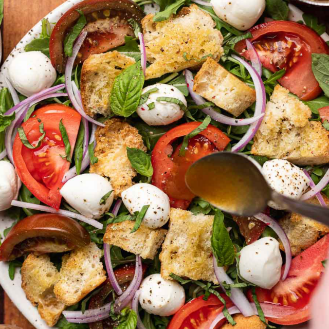 Dressing being poured onto green salad.