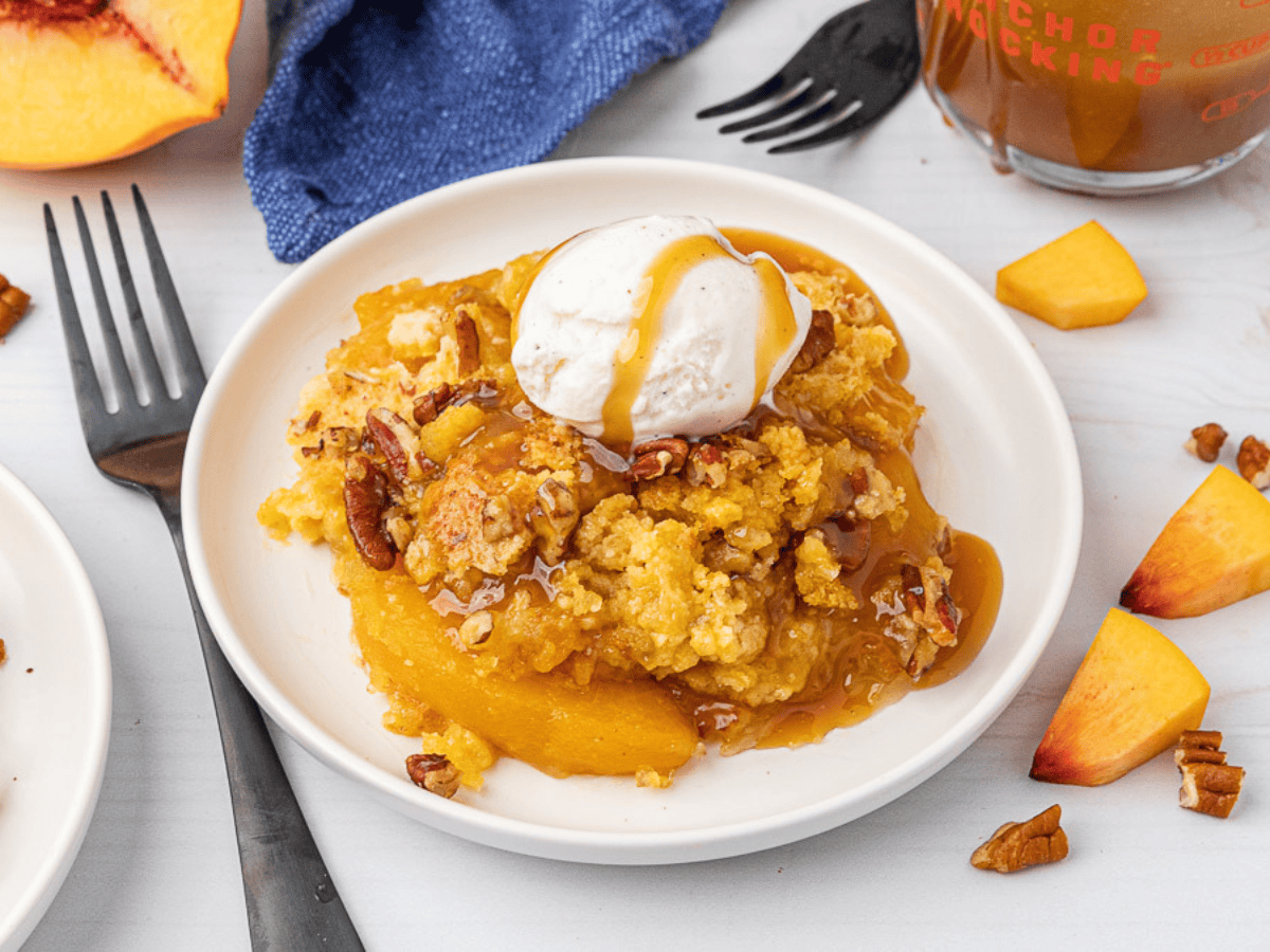 Tan colored dessert with pecans and peaches topped with ice cream on a white plate.