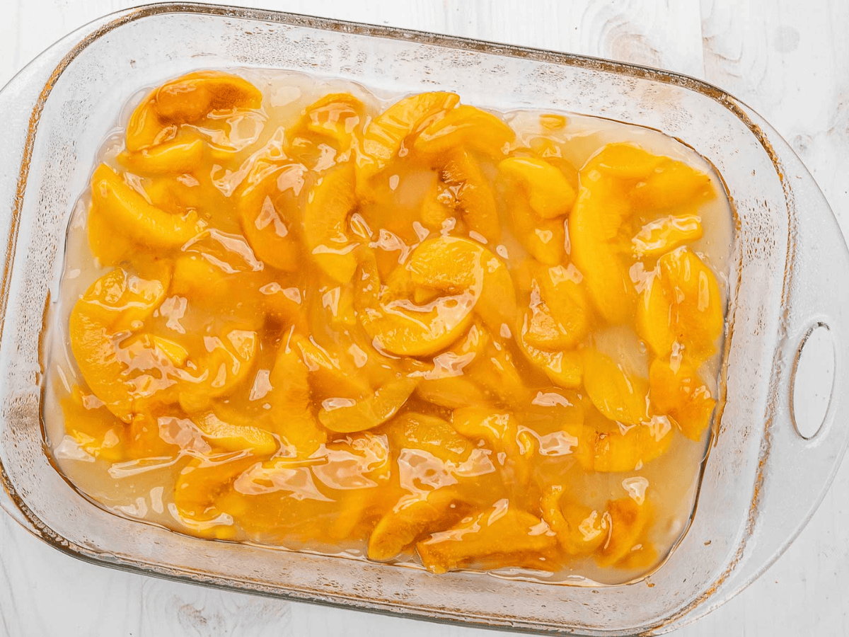 Orange colored fruit in glass baking dish in a liquid.
