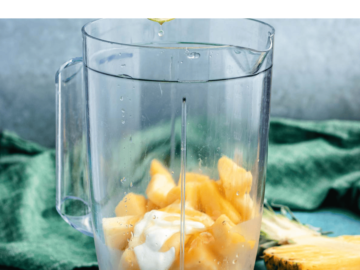 Lime juice being squeezed into blender with fruit.