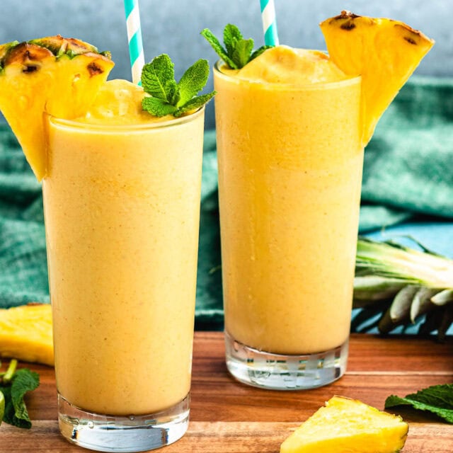 Two glasses of fruit smoothie with straws and garnish.