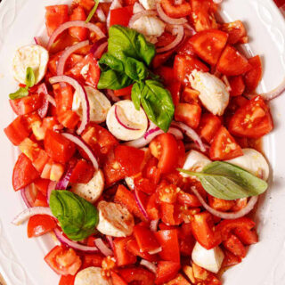 Large serving plate with tomato, mozzarella, and onion salad with basil garnish.
