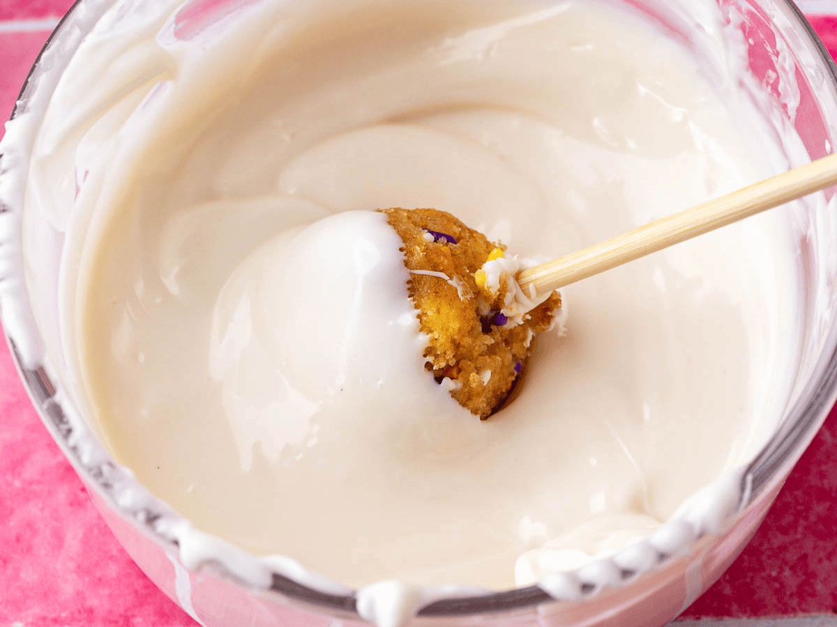 Small ball of cake being dipped in white chocolate.