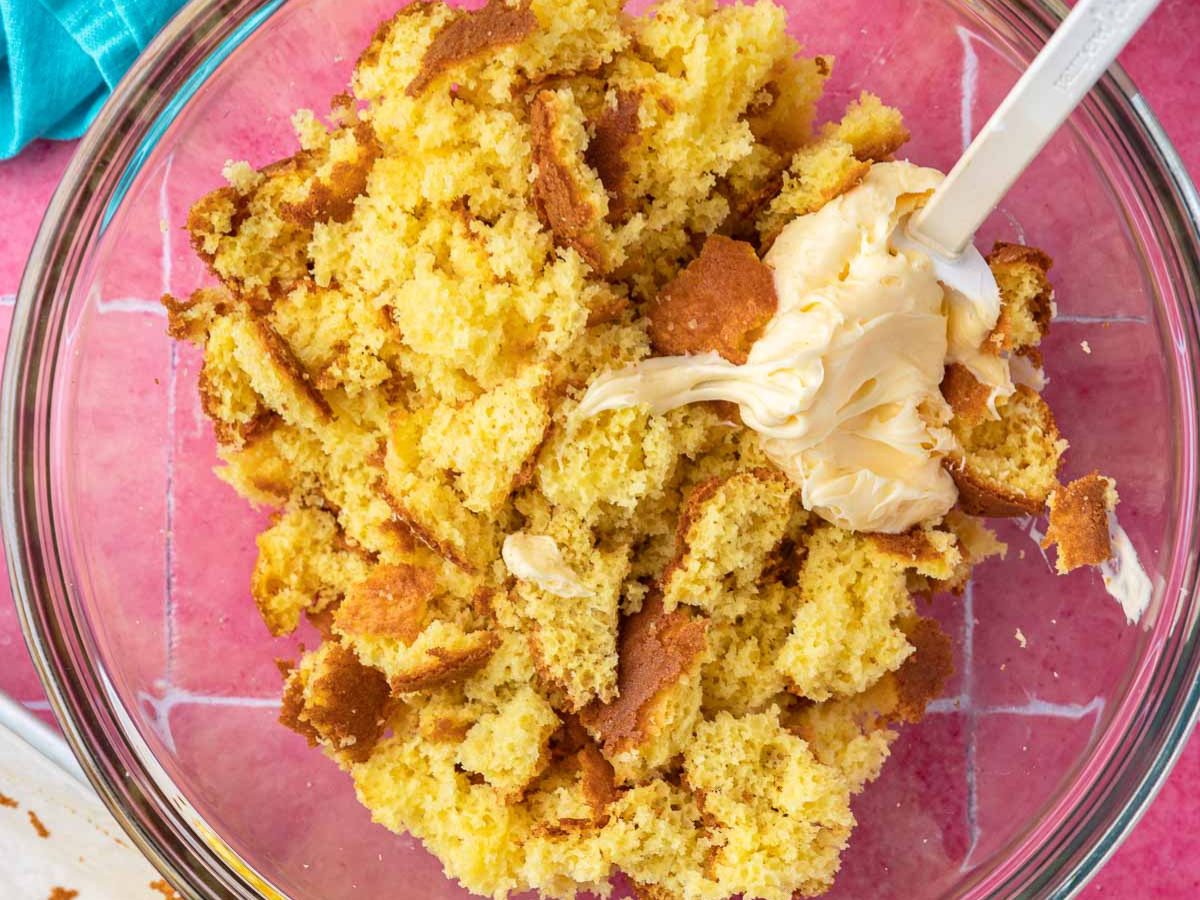 Crumbled up cake in a bowl with buttercream frosting.