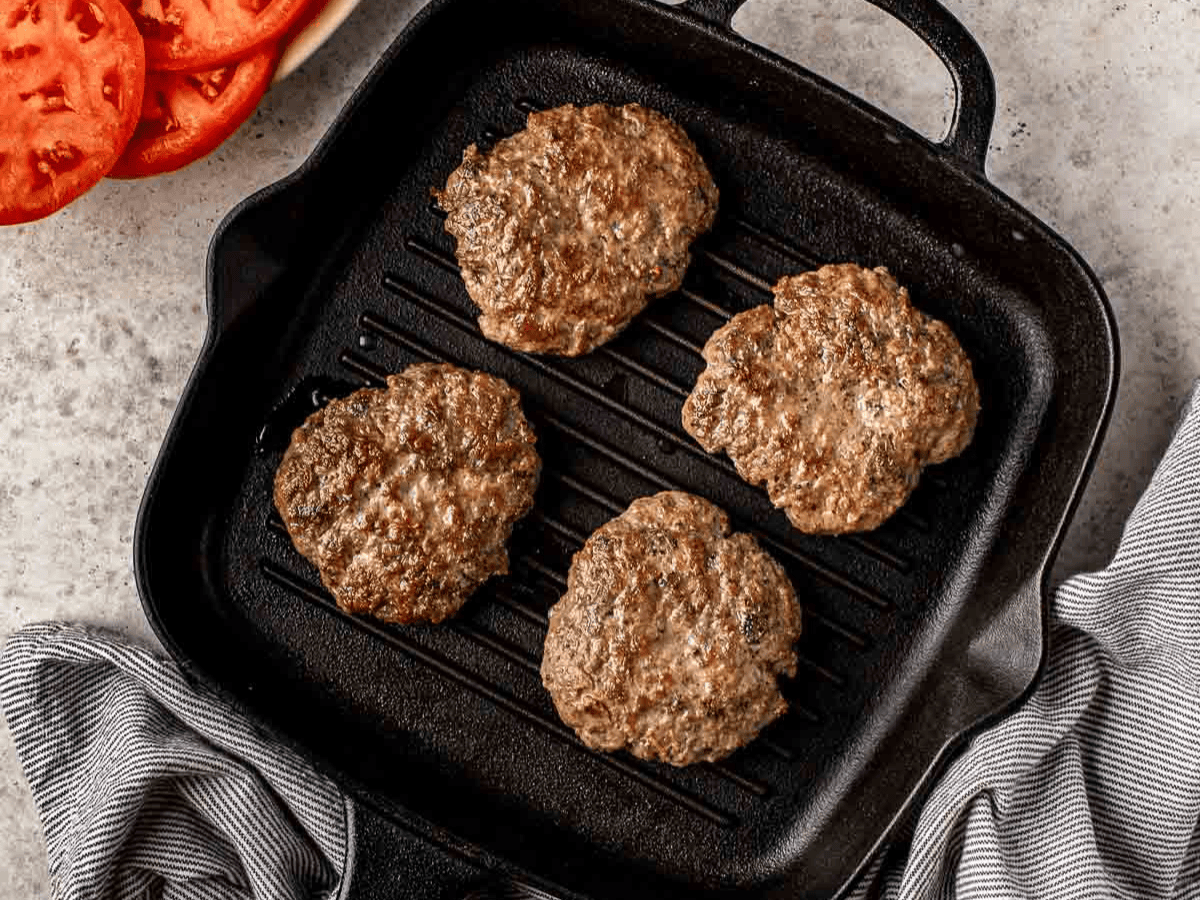 Four cooked burger patties in pan.