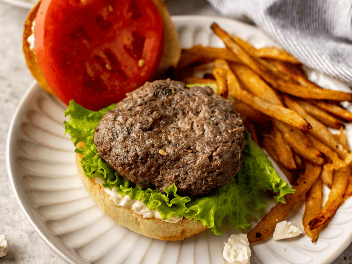 Dressed hamburger on dinner plate with fries.