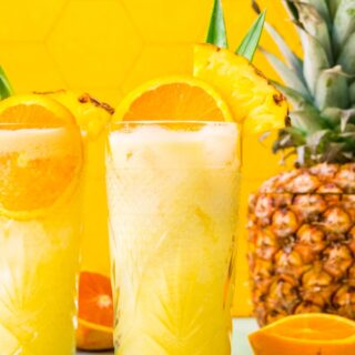 Two tropical drinks with orange and pineapple garnish.