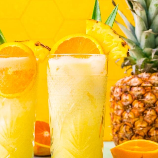 Two tropical drinks with orange and pineapple garnish.