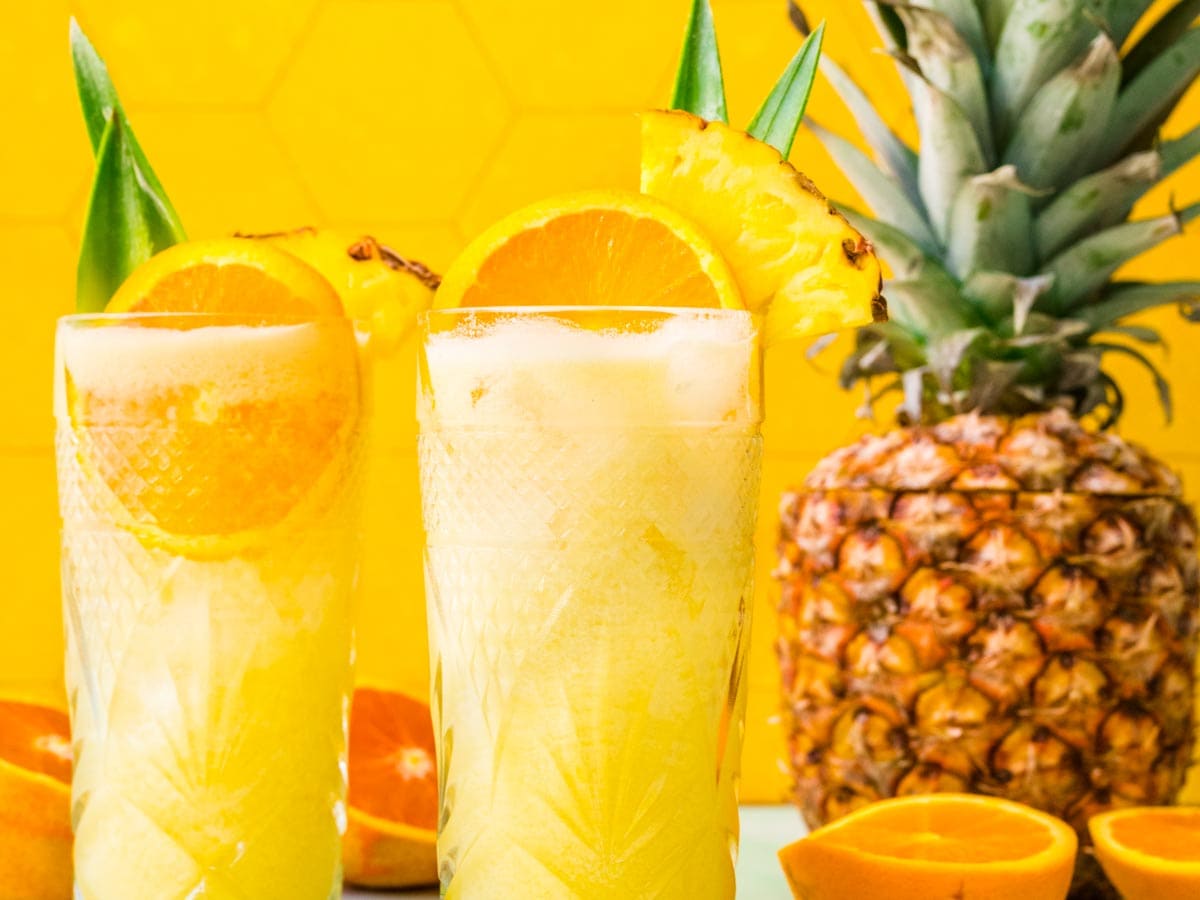 Two tropical drinks with orange and pineapple garnish.
