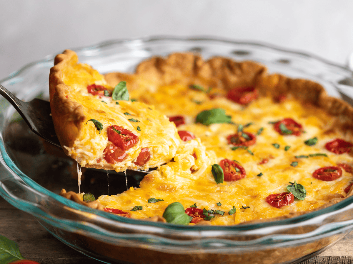 Finished savory pie in a glass pie tin with red fruit, spices, cheese and egg.