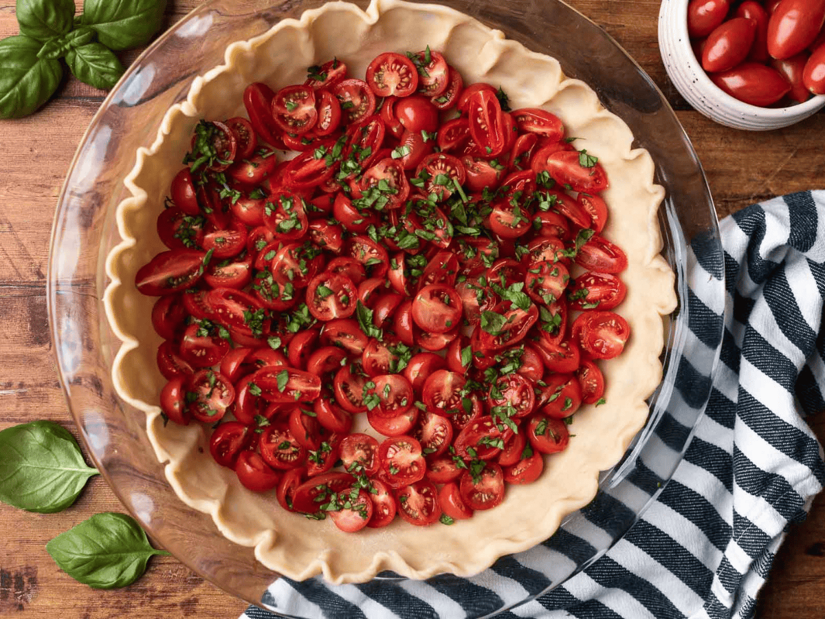 Uncooked pie crust in a glass pie dish with red fruit and spices.