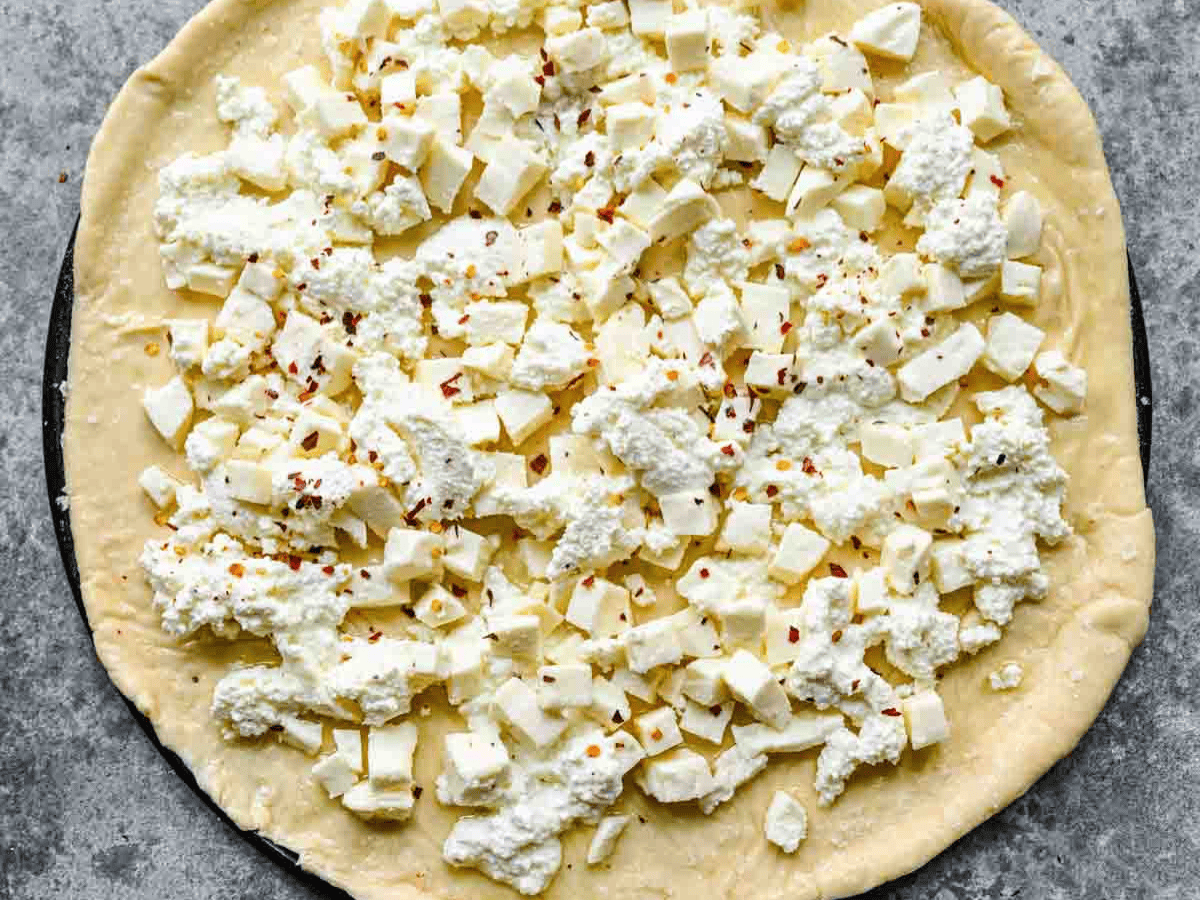 Raw pizza with cheese and red pepper flakes.