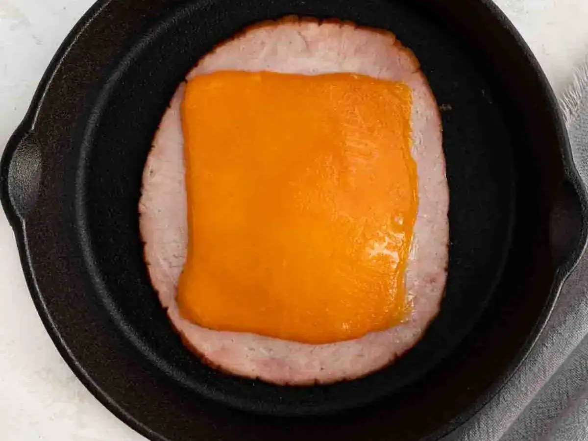 Slice of ham and cheese cooking in pan.