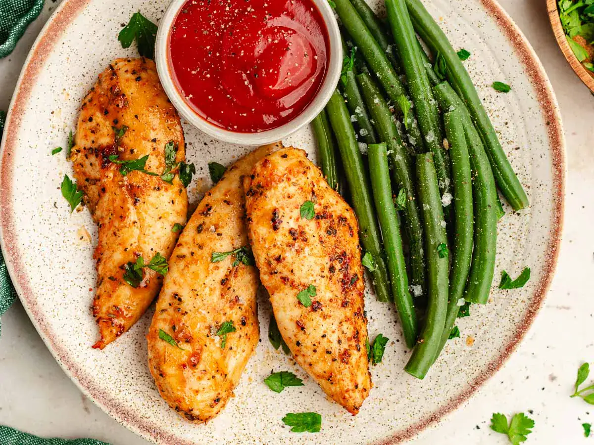 Seasoned and baked chicken with green beans on dinner plate.
