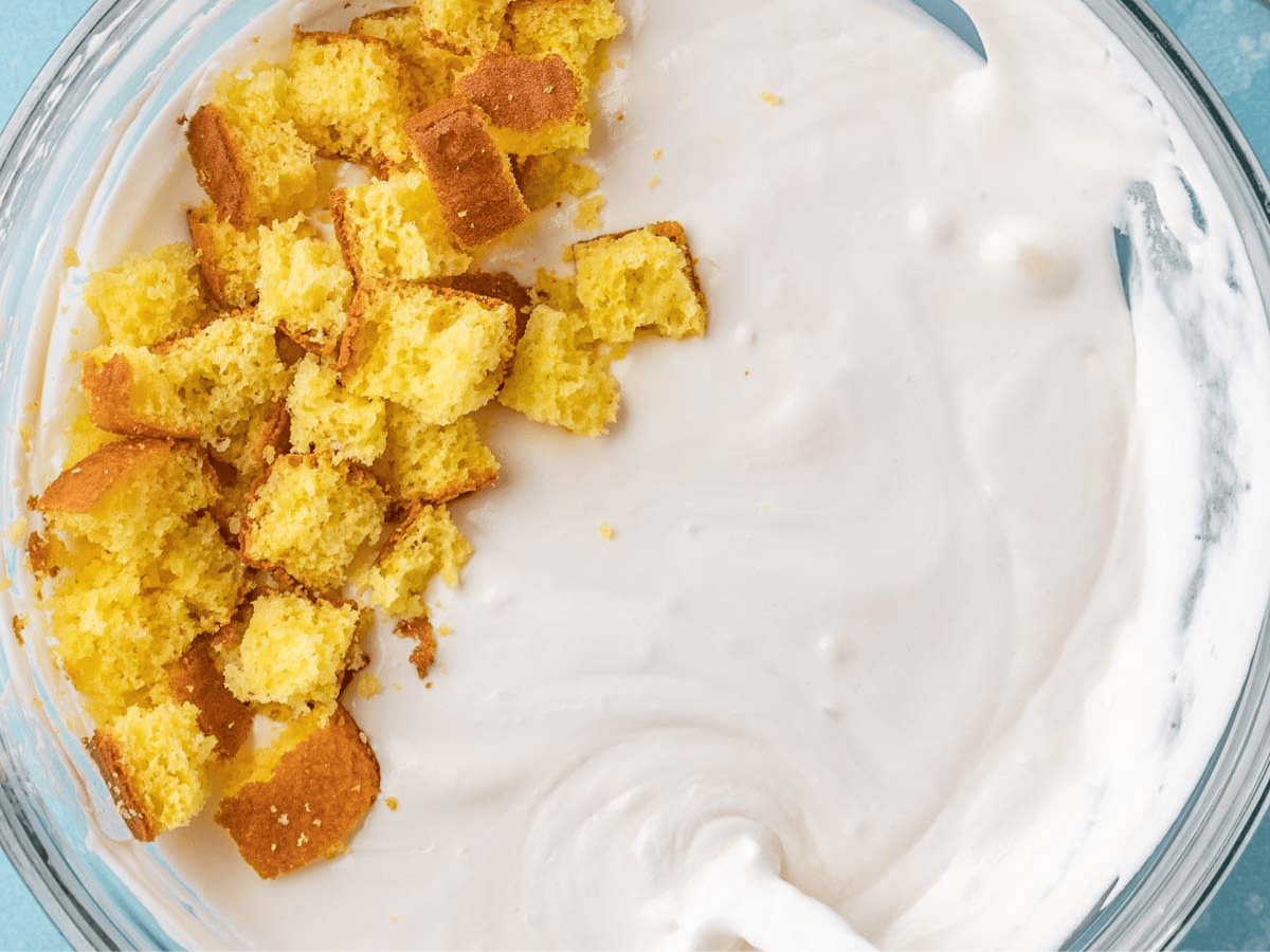 Cubed yellow cake, heavy cream, and condensed milk mixed in bowl.