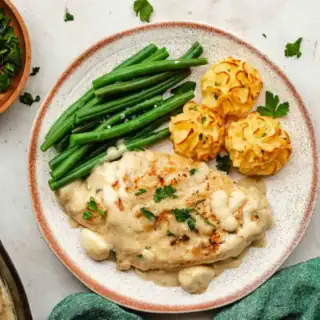Poultry dish on a white plate with a green vegetable and mashed potatoes.