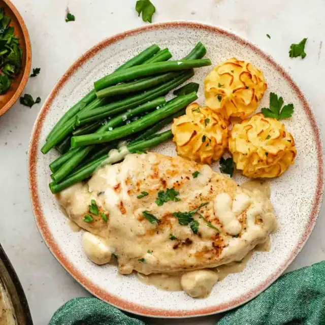 Poultry dish on a white plate with a green vegetable and mashed potatoes.