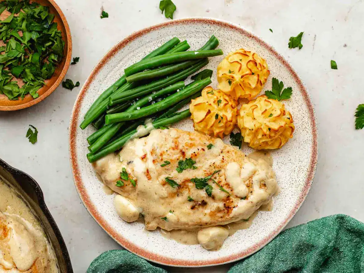 Poultry dish on a white plate with a green vegetable and mashed potatoes.