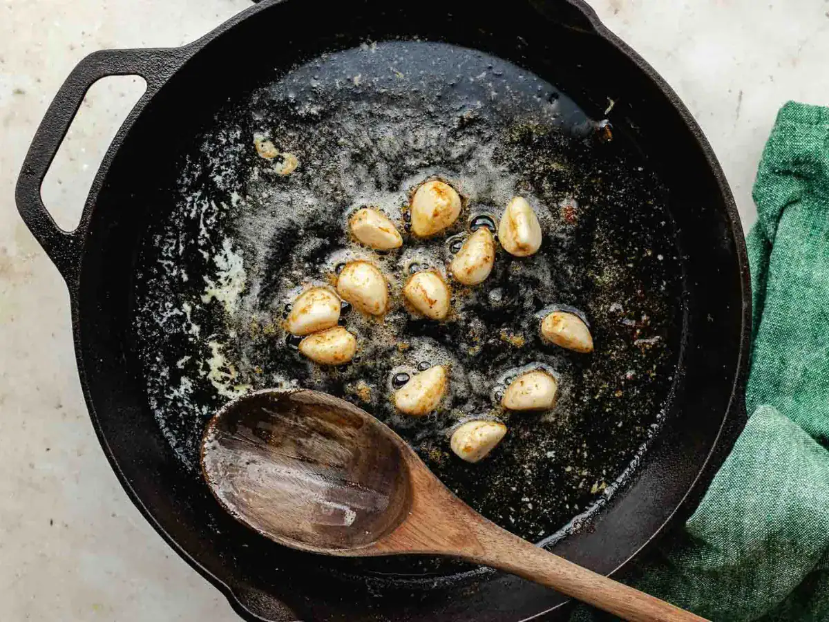 Garlic being cooked in a cast iron pan.