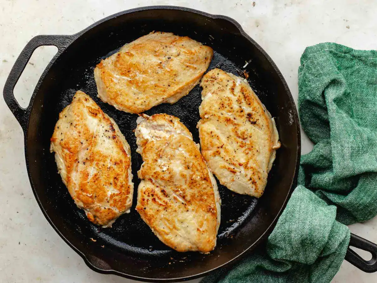 Poultry being cooked in a cast iron pan.
