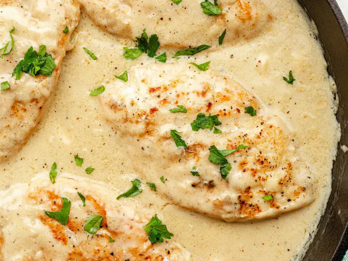 Close up of a poultry dish cooked in a tan sauce garnished with a green herb.