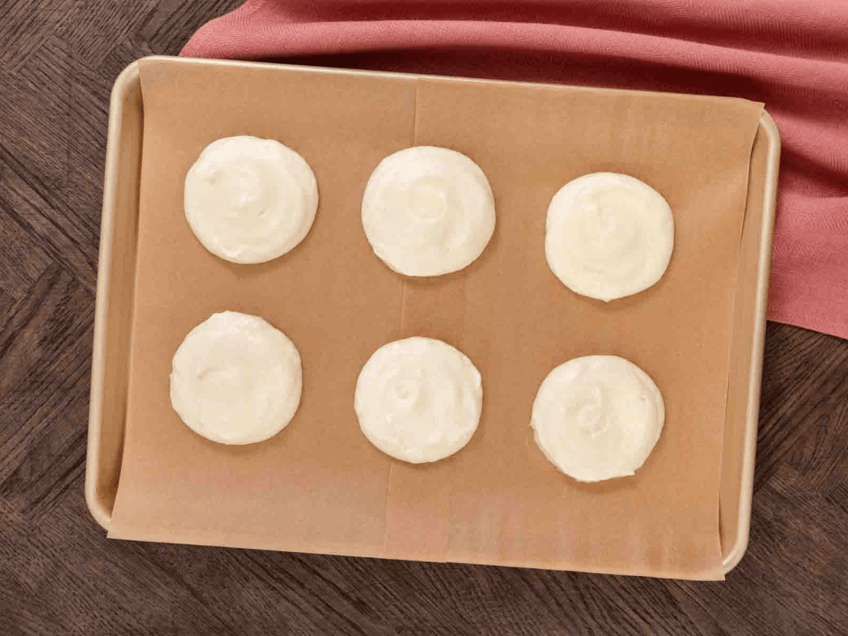 Baking tray with a mixture of round cream colored dough spread into 6 servings.