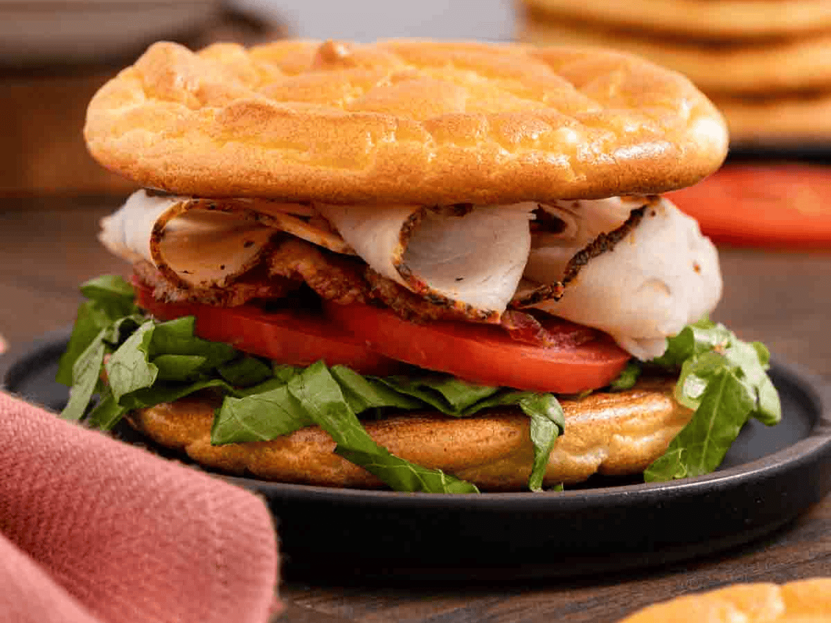 White meat, tomatoes, and lettuce sandwiched between round tanned colored bread.