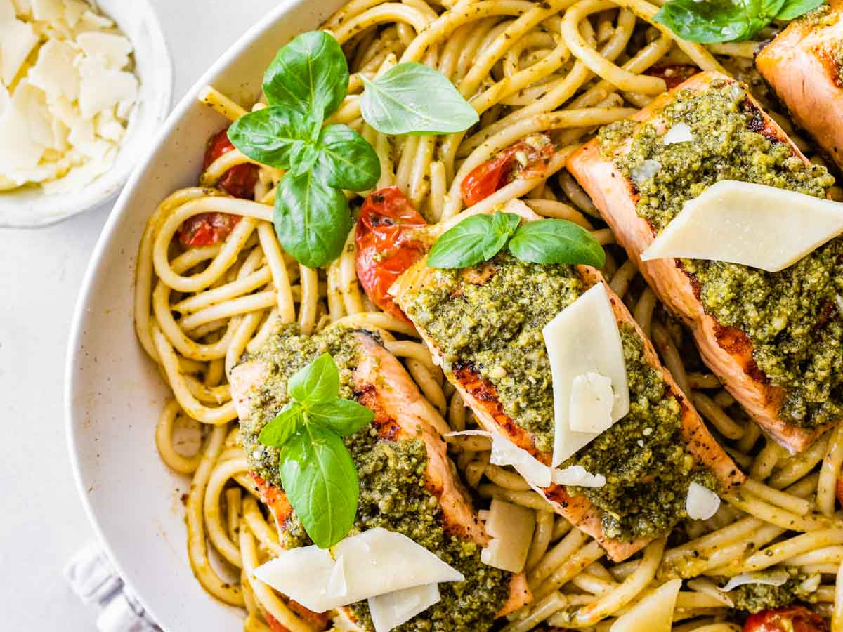 Fish on top of a bed of pasta with green garnish.