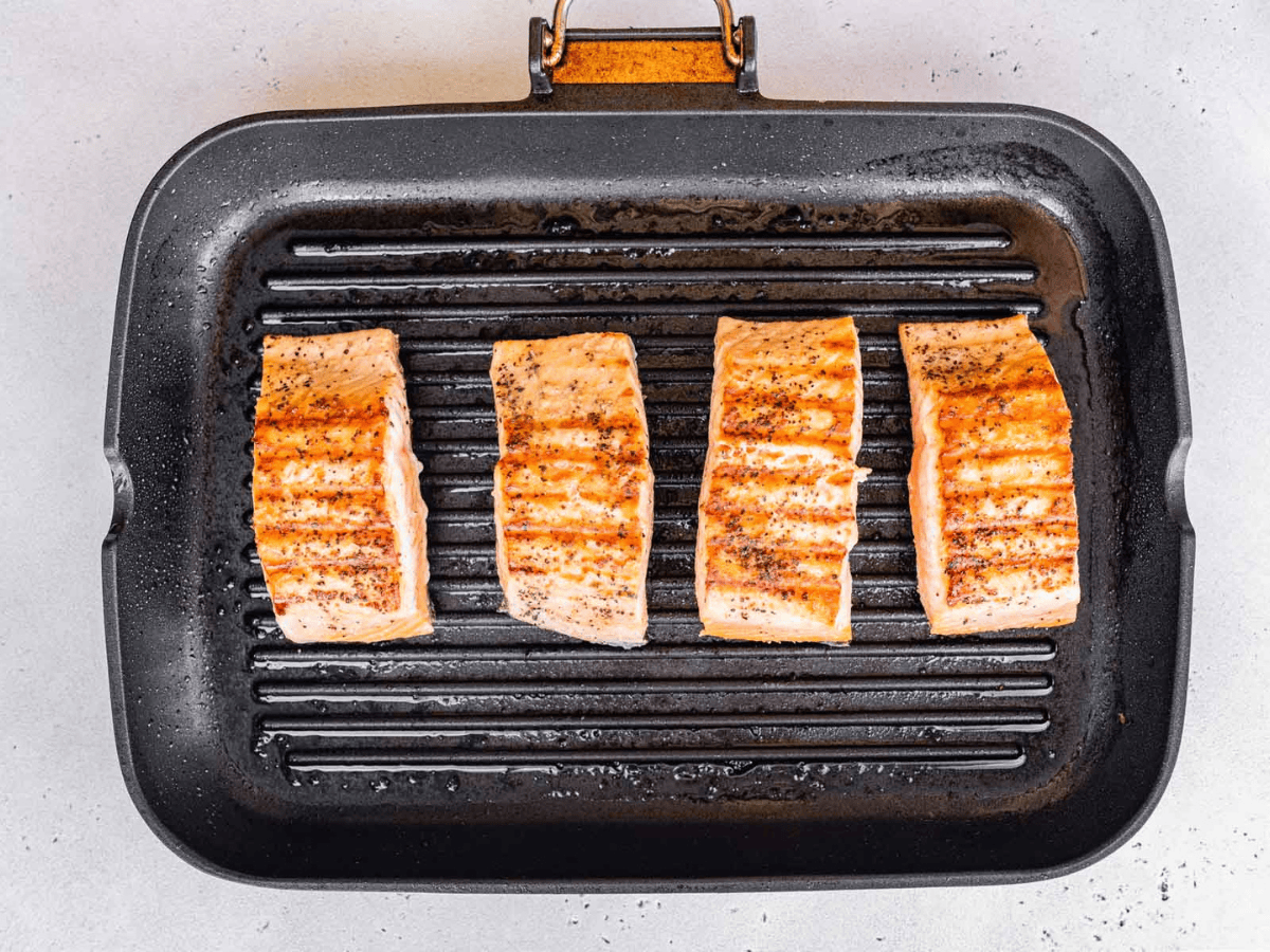 A rectangle pan with 4 filets of pink fish being grilled.