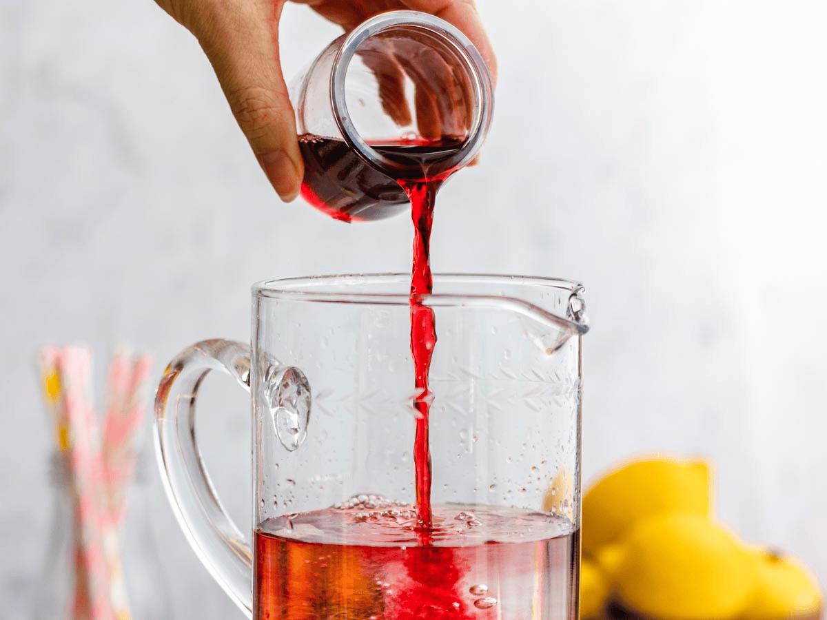 Red colored liquid being poured into a glass pitcher.