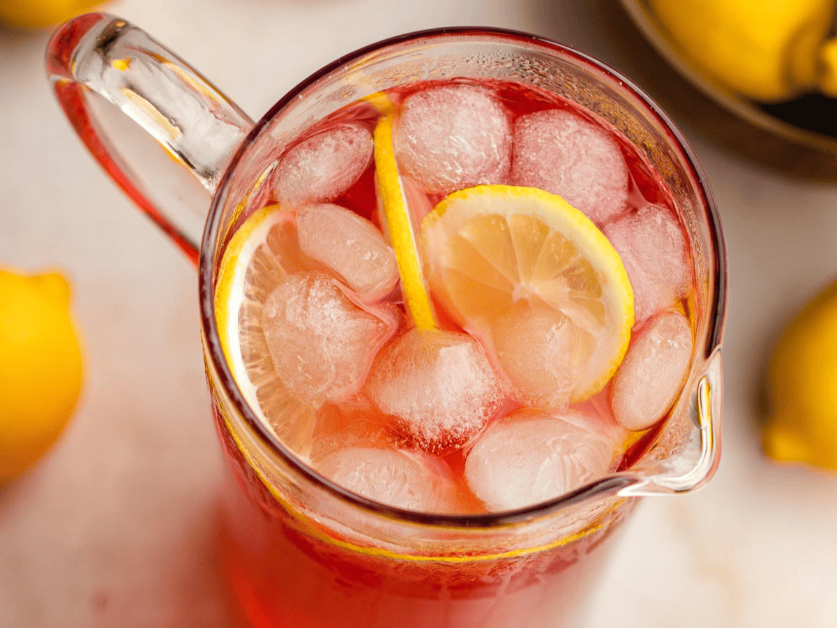 Top view of a glass pitcher filled with a rose colored liquid with ice and lemon wedges.