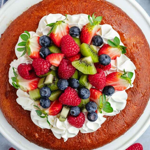 Overhead view of a cake topped with fruit and whipped cream.